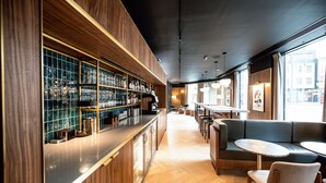 A modern bar area with wooden paneling, a counter with glassware, and seating with round tables.