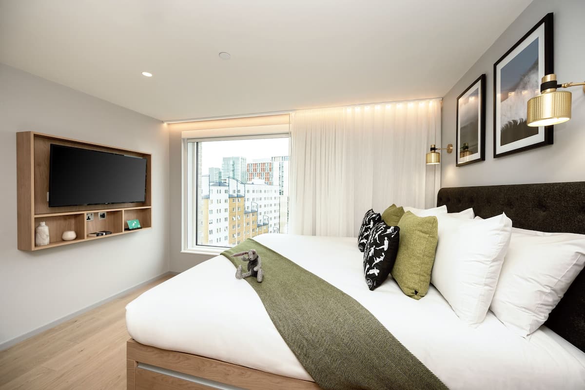 Une chambre d’hôtel moderne dotée d’un grand lit, d’un téléviseur fixé au mur, d’une vue sur la ville et d’une fenêtre avec des rideaux.