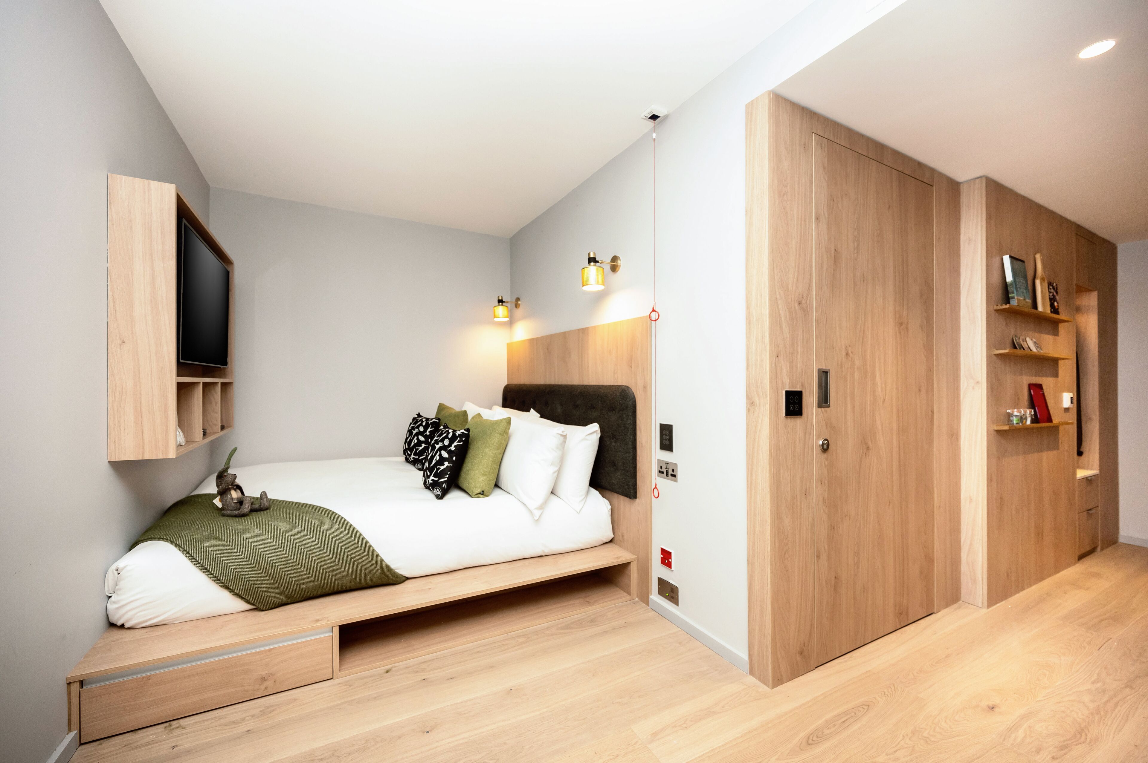 A modern bedroom with a bed, built-in shelving, a TV, and a wardrobe.