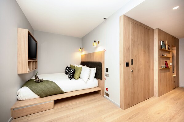 A modern bedroom with a bed, built-in shelving, a TV, and a wardrobe. - Wilde Aparthotels, London, Aldgate Tower Bridge (London)