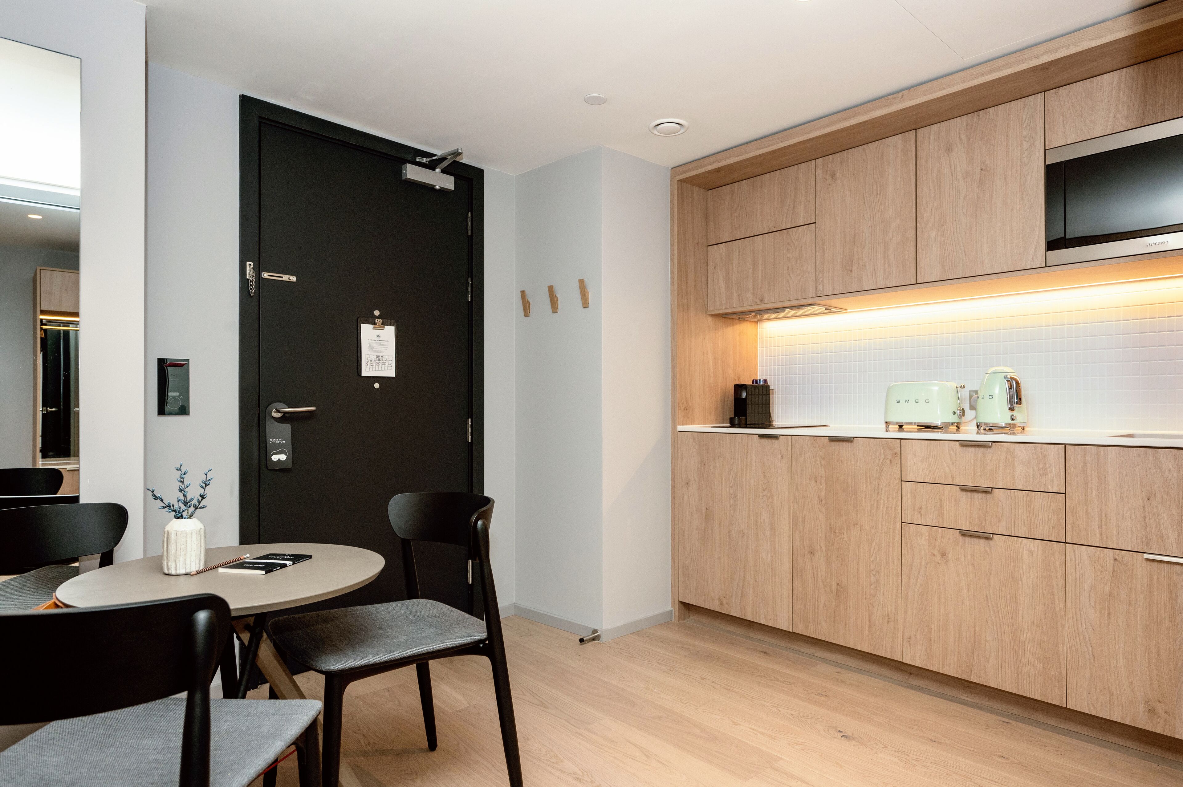 A modern kitchen with wooden cabinets, a black door, and a round dining table with chairs.