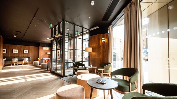 A modern hotel lobby with wooden paneling, large windows, and comfortable seating areas.