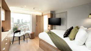 A modern hotel room with a large bed, a TV, a desk, and a chair.