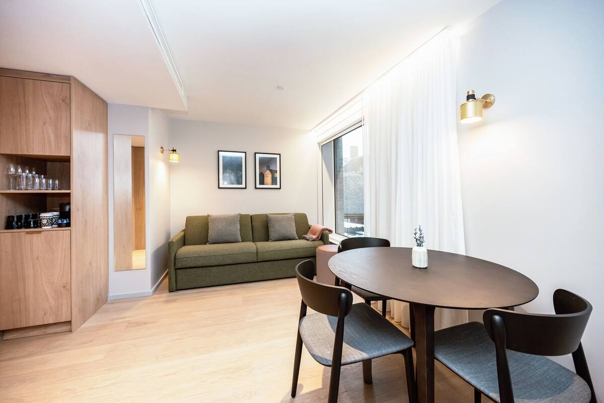 Un salon moderne avec un meuble en bois, un canapé vert, une table à manger avec des chaises et une grande fenêtre avec des rideaux.