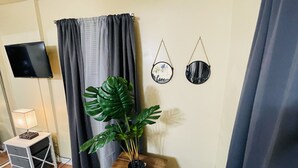 Una habitación con televisión, planta, mesita de madera, lámpara y dos adornos en la pared.