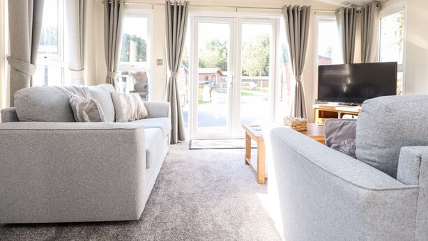 Ein modernes Wohnzimmer mit grauen Sofas, einem Flachbildfernseher und einer großen Schiebeglasdoor, die zu einem Außenbereich führt.