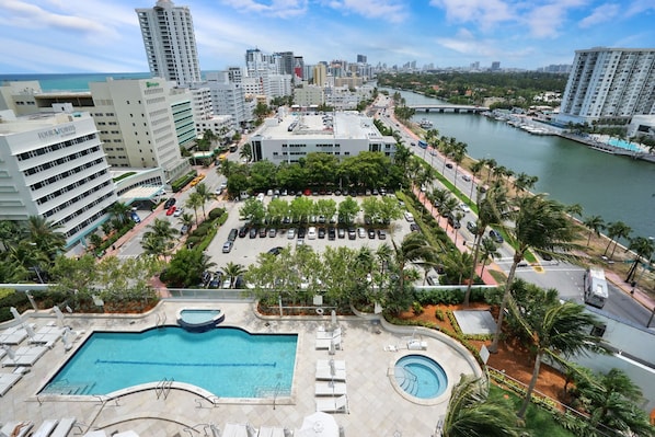 A hotel with a swimming pool, a parking lot, and a view of the cityscape.
