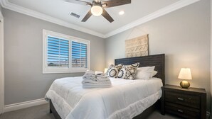 Quarto com uma cama, mesa de cabeceira, abajur, ventilador de teto e janela com persianas.