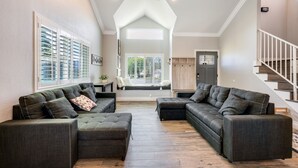 Uma sala de estar espaçosa com dois sofás cinza escuro, piso de madeira e uma escada para um andar superior.