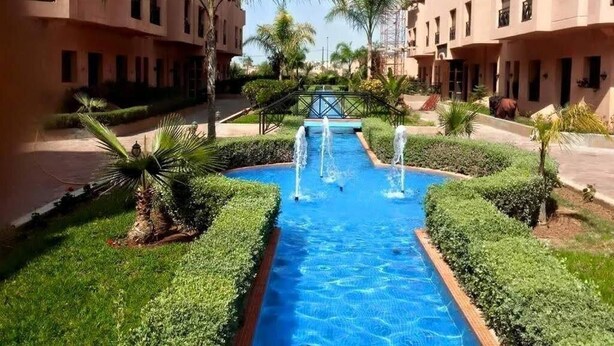 A courtyard with a central water feature, surrounded by well-maintained greenery and buildings with balconies.