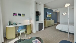 A hotel room with a bed, a desk with a chair, a kitchenette, and a TV. - Ocean & Bay Junior Suite in the Fontainebleau (Miami Beach)