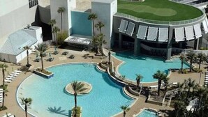 Un hotel con una grande piscina centrale, palme e un campo da tennis.