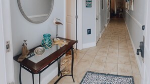 Un corridoio con un mobile consolle in legno, uno specchio rotondo e una decorazione a stella marina. Si vedono porte che conducono ad altre stanze e un cartello appeso al muro.