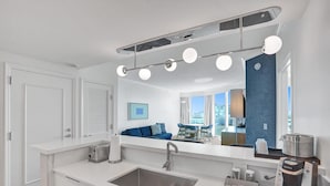 Un baño moderno con un espejo grande, un lavamanos, una cafetera y vistas a la ciudad a través de amplios ventanales.
