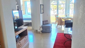Ett rymligt vardagsrum med tv, sittmöbler och utsikt genom ett stort fönster.