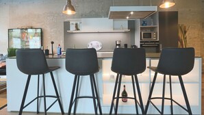 A modern kitchen with a bar area, featuring three black bar stools, a television, and various kitchen appliances. - Luxury Loft Sylt - your special vacation home (Westerland)