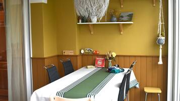 Een eetruimte met een tafel voor vier personen, houten stoelen, een hanglamp en een plank met decoratieve objecten.