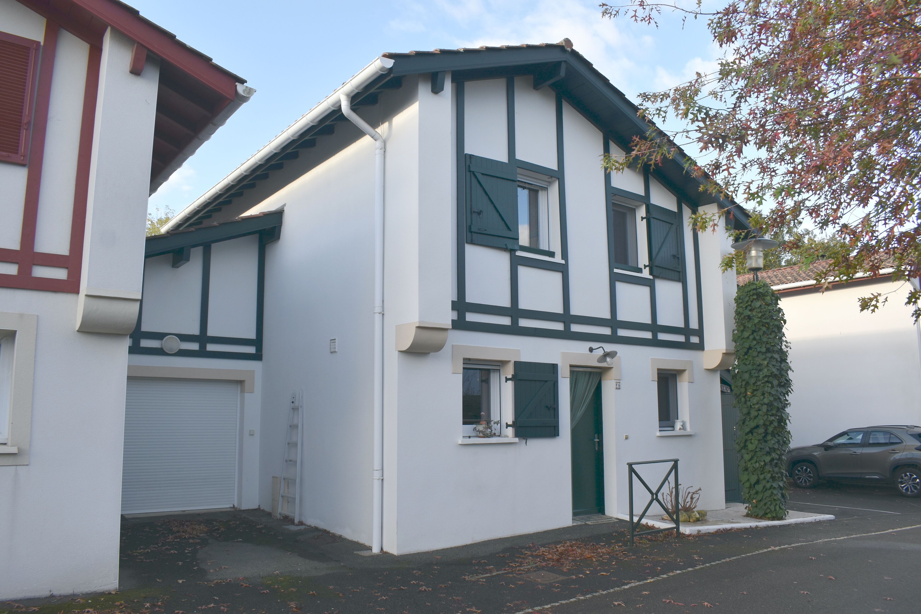 Een gebouw met twee verdiepingen, met een witte gevel en donkere accenten, een garage deur, een klein raam en een deur met een groen gordijn.