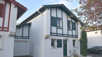 Een gebouw met twee verdiepingen, met een witte gevel en donkere accenten, een garage deur, een klein raam en een deur met een groen gordijn.