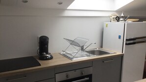 Uma cozinha compacta com forno embutido, cafeteira e pia com escorredor.