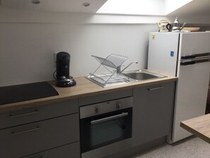 Une cuisine compacte équipée d’un four encastré, d’une machine à café et d’un évier avec un égouttoir.
