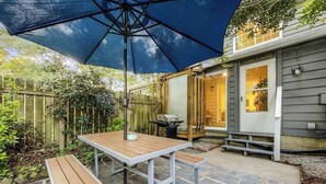 An outdoor patio with a wooden table and bench, a large blue umbrella, and a stone-tiled floor. - 5 Min to Beach, Renovated Townhome (Mount Pleasant)