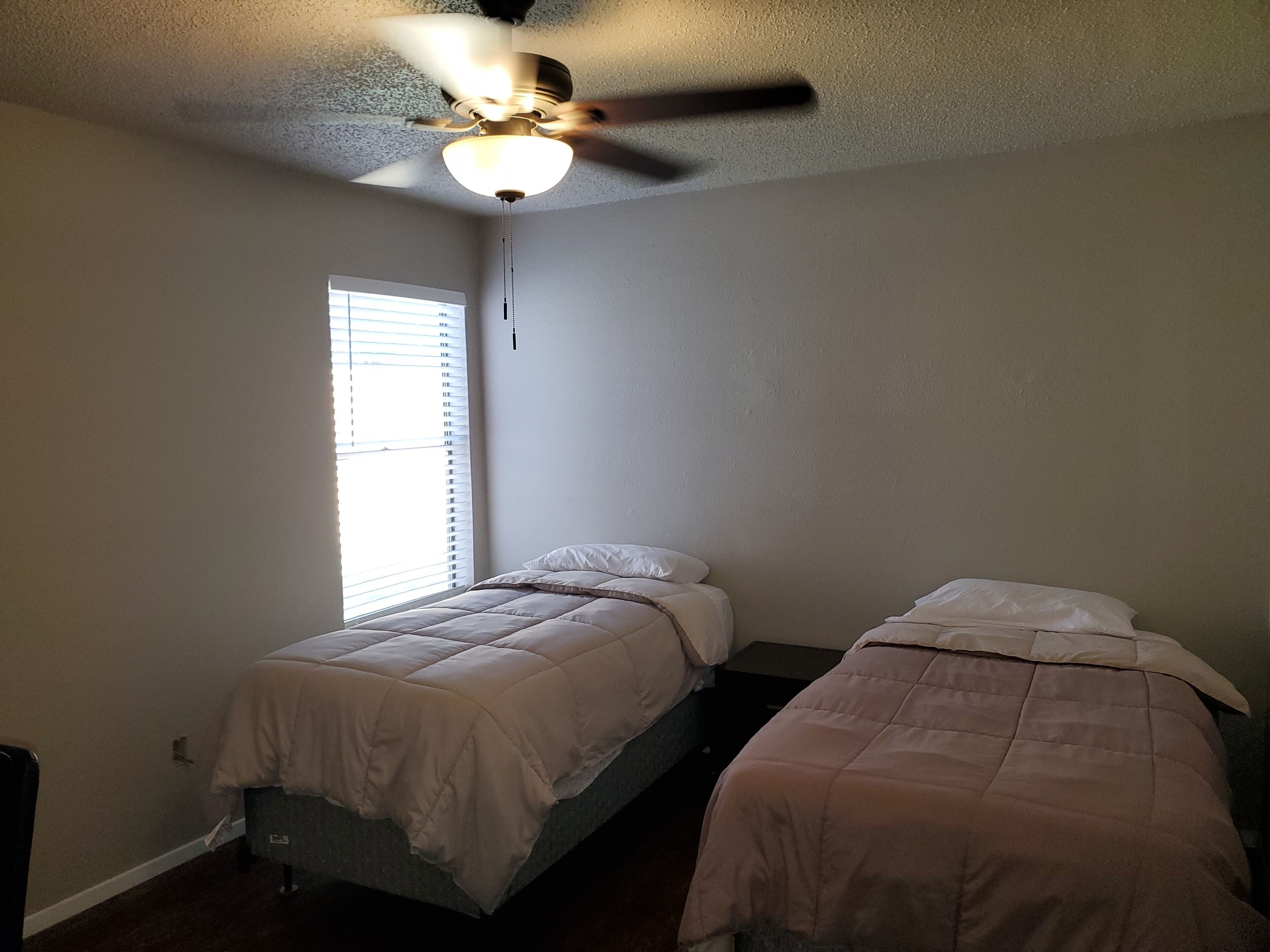 Un dormitorio con dos camas, ventilador de techo y ventana con persianas.