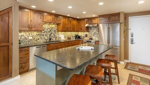 A kitchen with wooden cabinets, a granite countertop, a stainless steel refrigerator, and a built-in island with stools. - Beautiful Condo in the Pines, Mountain Views, Shared Pool & Hot Tub (Keystone)