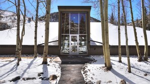 A building with a glass door entrance, surrounded by snow-covered ground and birch trees. - Beautiful Condo in the Pines, Mountain Views, Shared Pool & Hot Tub (Keystone)