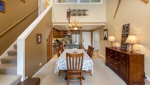 A spacious dining area with a high ceiling, a chandelier, and a wooden dining table with chairs. - Beautiful Condo in the Pines, Mountain Views, Shared Pool & Hot Tub (Keystone)