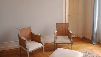 Una habitación con dos sillones de mimbre, un reposapiés blanco y una alfombra estampada sobre piso de madera.