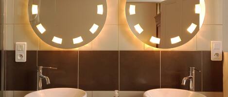A bathroom with two large white sinks, a mirror above each, and a wall-mounted light fixture.