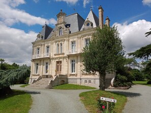 A grand, historic building with multiple stories, a prominent entrance with steps, and a well-maintained garden. - Château du Breuil (Beaulieu-sur-Layon)