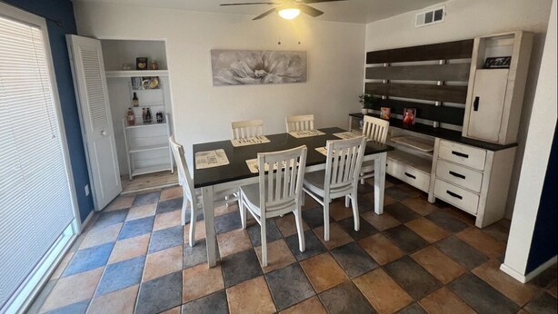 Une cuisine de taille réduite comprenant une table à manger, des chaises, un ventilateur de plafond et un réfrigérateur.