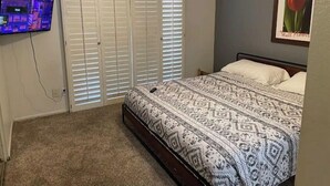 Une chambre à coucher avec un lit, un ventilateur de plafond, un téléviseur fixé au mur et un tableau représentant une tulipe.