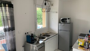 Eine kompakte Küche mit Geschirrspüler, Mikrowelle und Kühlschrank. Über der Spüle befindet sich ein Fenster, das teilweise von einem Vorhang verdeckt wird.