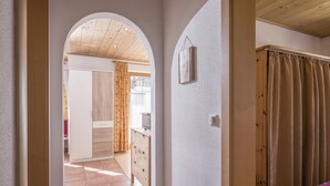 A hallway with a wooden wardrobe, a bed with a curtain, and a kitchen area in the background. - Apartment 1 minute from the ski lift (Brixen im Thale)