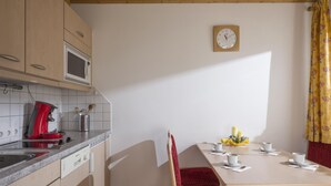 A kitchen with a coffee maker, microwave, and utensils on the counter. There is a dining table with chairs and a clock on the wall. - Apartment 1 minute from the ski lift (Brixen im Thale)