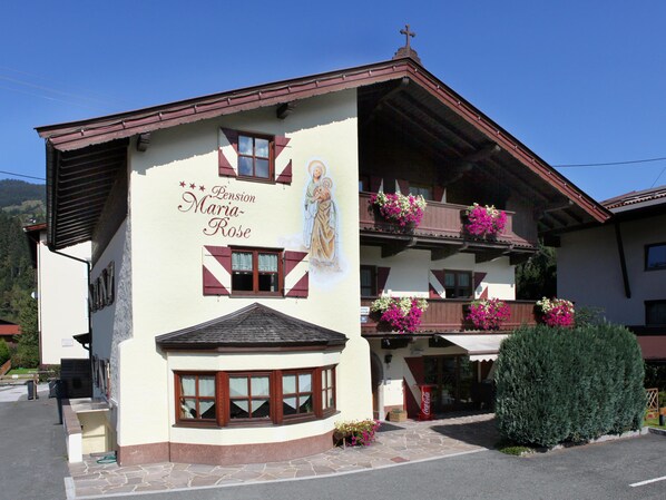 A building with a mural of a religious figure, a Coca-Cola sign, and flower boxes on balconies. - Holiday home near ski lift (Kirchberg in Tirol)