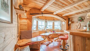 Ein rustikales Holzhaus-Interieur mit Holztisch und -bänken, einem Fenster mit Vorhängen und einer Wanduhr.