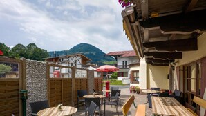 Eine Terrassengaststätte mit Steinboden, Holztischen und Korbstühlen.