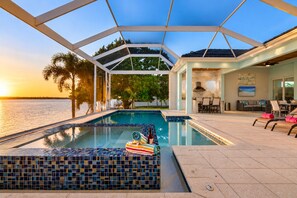 A swimming pool with a tiled deck, a covered patio area, and a view of the water.