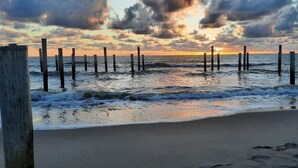 Uma praia com estacas de madeira na água, ondas e um pôr do sol.
