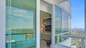 Un appartement situé dans un immeuble de grande hauteur, doté d’un balcon, offrant une vue sur la ville, et présentant un intérieur moderne avec un bureau et une chaise.