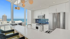 Une cuisine moderne dotée d’un grand îlot central, d’appareils électroménagers en acier inoxydable et offrant une vue sur la ville et l’océan.