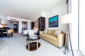 A modern hotel room with a sofa, a dining area, and a large window. - Sorrento Ocean / Bay Jr Suite in the Fontainebleau (Miami Beach)