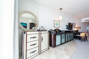A modern kitchen with a large round mirror, a built-in bar, and a dining area with chairs. - Sorrento Ocean / Bay Jr Suite in the Fontainebleau (Miami Beach)