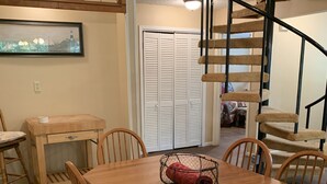 A dining area with a wooden table and chairs, a small side table, a framed picture on the wall, and a staircase with a black railing. - Two story home with Las Moras Creek views (Brackettville)