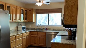 A kitchen with wooden cabinets, a stainless steel refrigerator, a microwave, a sink, and a ceiling fan. - Two story home with Las Moras Creek views (Brackettville)