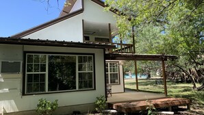 A two-story house with a large window, a wooden deck, and a covered patio area. - Two story home with Las Moras Creek views (Brackettville)